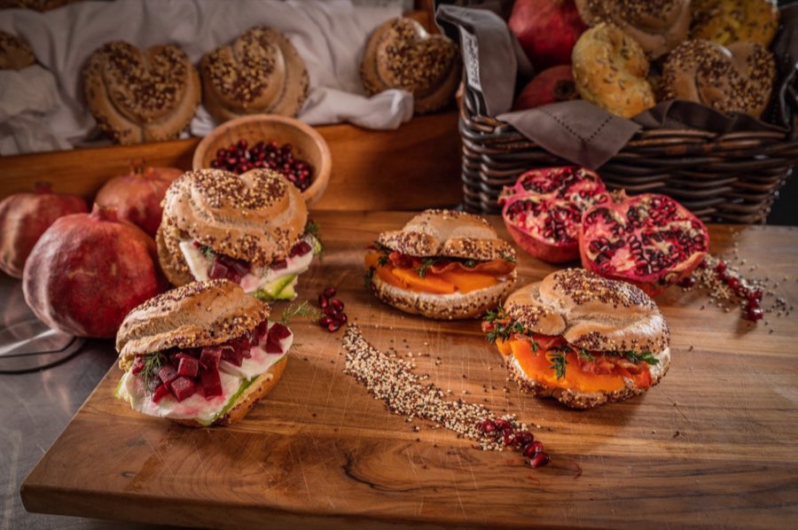 Assortimento di bagel farciti, melagrane e semi su tavolo in legno